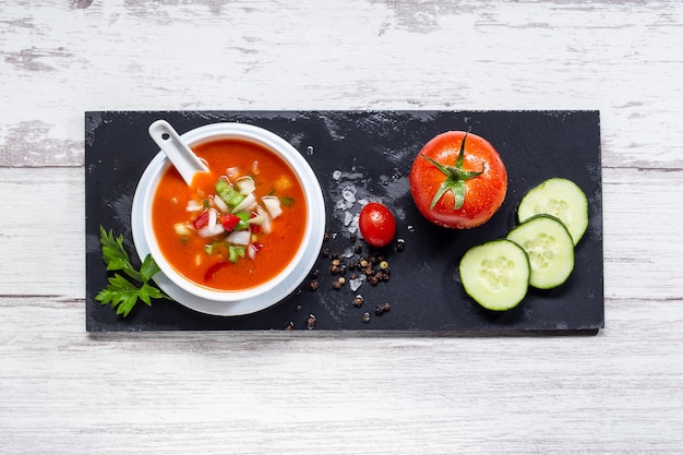 Gazpacho. Sopa de tomate tradicional española con tomates frescos, pepino fresco y aceite de oliva, sobre base de madera blanca.