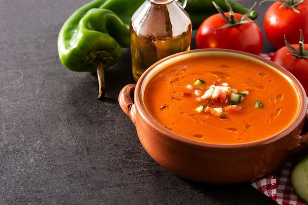 Gazpacho-Suppe im Topf und Zutaten auf schwarzem Schiefertisch