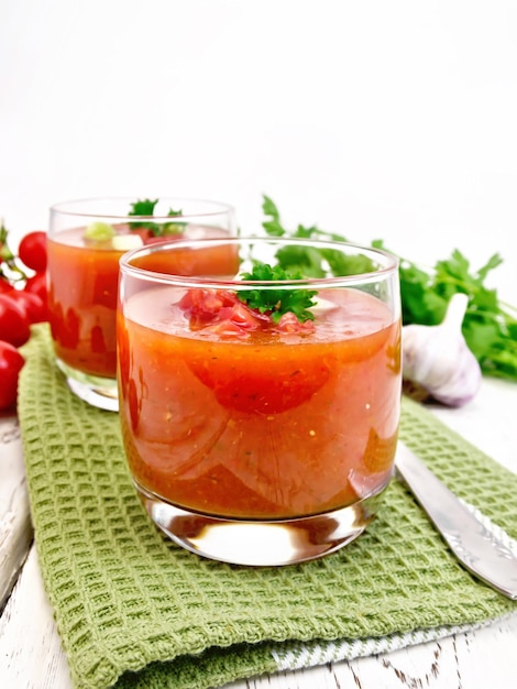 Gazpacho-Tomatensuppe in zwei Gläsern mit Petersilie und Gemüse auf der grünen Serviette auf den hellen Holzbrettern des Hintergrundes