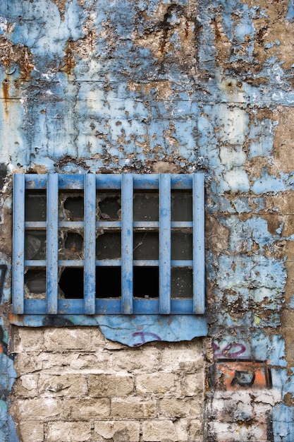 Gealterte verwitterte Backsteinmauer mit Graffiti und blauem Fenster