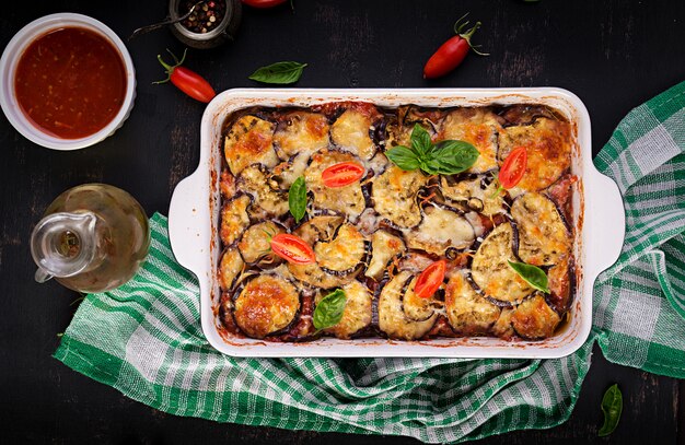 Gebackene Aubergine mit Käse auf einem dunklen Holztisch. Parmigiana melanzane. Ansicht von oben. Italienische Küche.