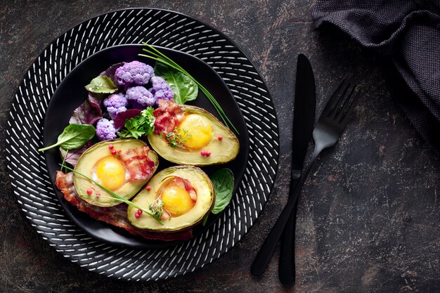 Gebackene Avocado mit Ei und Speck flach auf dunkel legen