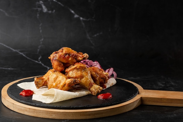 Gebackene Buffalo Chicken Wings mit Sesam, Zwiebeln und Chili-Scheiben auf schwarzem Holzbrett.