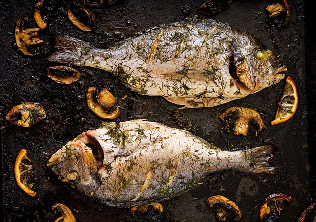 Gebackene Dorado-Fische in Knoblauch-Dill-Sauce mit Champignons und Zitrone.