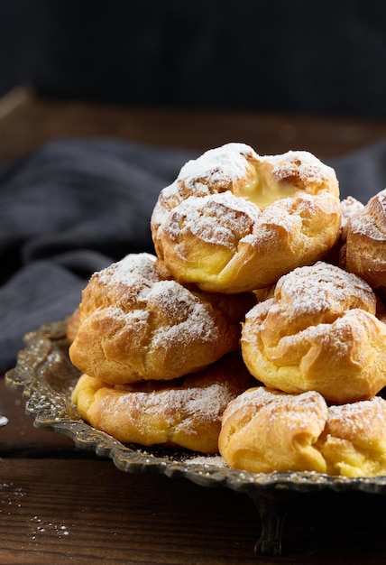 Gebackene eclairs mit puddingcreme auf einer runden metallplatte, die mit puderzucker bestreut ist