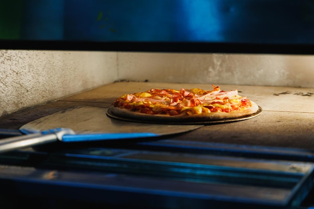 Gebackene frische Pizza mit einem Metallspatel aus dem Ofen nehmen