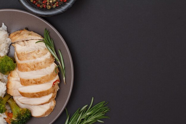 Gebackene Hähnchenbrust oder Filet auf Teller, Glasschüssel mit Pimentbeeren und Rosmarin auf schwarzem Hintergrund. Ansicht von oben.