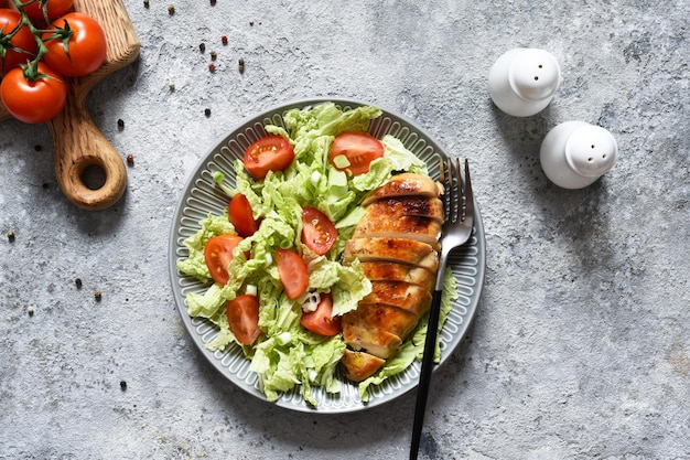 Gebackene Hähnchenbrust und Salat mit Tomaten auf Betongrund. Gesunde Ernährung, Keto-Diät, Paleo-Diät. Draufsicht mit Kopienraum.