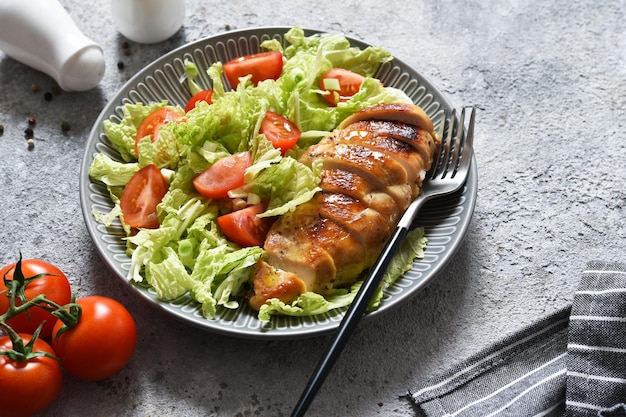 Gebackene Hähnchenbrust und Salat mit Tomaten auf Betongrund. Gesunde Ernährung, Keto-Diät, Paleo-Diät. Draufsicht mit Kopienraum.