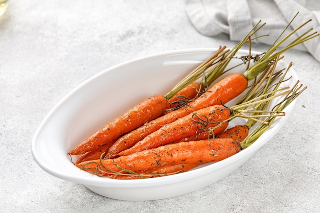 Gebackene Karotten mit grünen Spitzen in Auflaufform auf grauem Hintergrund Gesundes veganes Essen