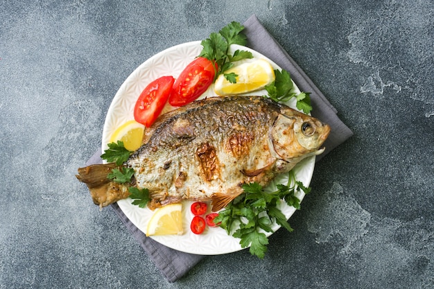 Gebackene Karpfenfische mit Gemüse und Gewürzen auf einer Platte auf einer dunklen Tabelle mit einer Kopie des Raumes.