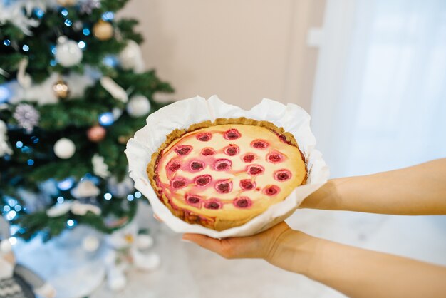 Gebackene Kirschpastete in den Händen neben Weihnachtsbaum