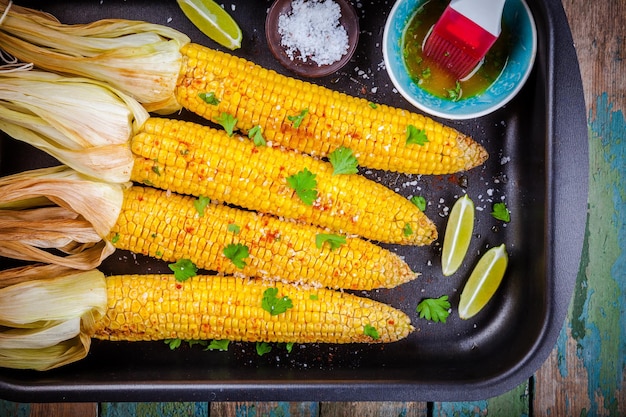 Gebackene Maiskolben mit Kräuterbutter und Kalk auf Holztisch