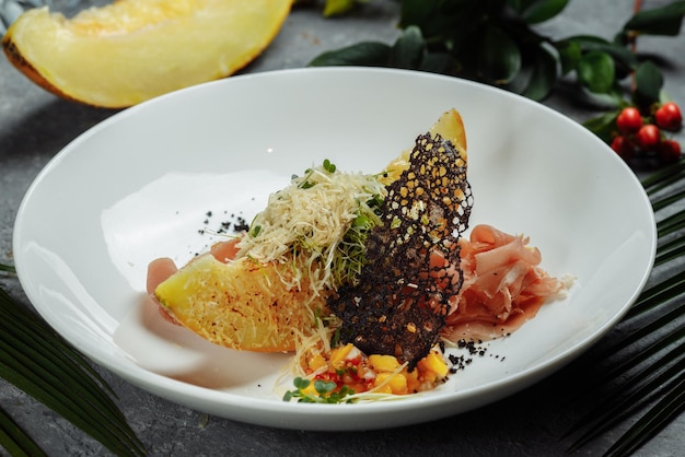 Gebackene Melone mit Parmesan und Jamon auf einem weißen Teller