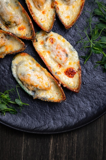 Gebackene Muscheln mit Käse auf einem dunklen Teller mit Kräutern und Zitrone auf Holzhintergrund