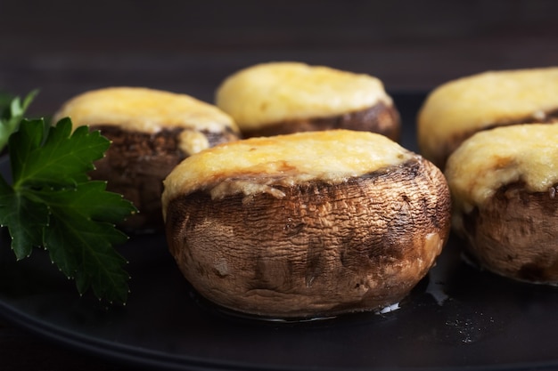 Gebackene Pilze gefüllt mit Käse und Kräutern auf einem schwarzen Teller. Holztisch.