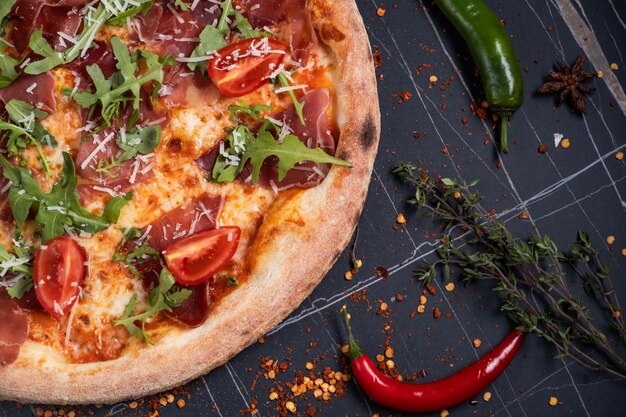 Foto gebackene pizza mit salami-prosciutto und huhn mit roter soße und geschmolzenem käse auf einem schwarzen holzgrund in einer komposition mit zutaten top-view