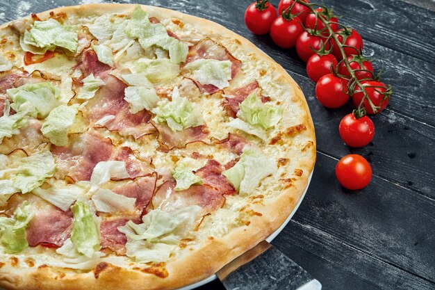 Gebackene Pizza mit Salat, Croutons, weißer Sauce und Hühnchen. Pizza Caesar auf einem schwarzen Holztisch in einer Komposition mit Zutaten. Draufsicht