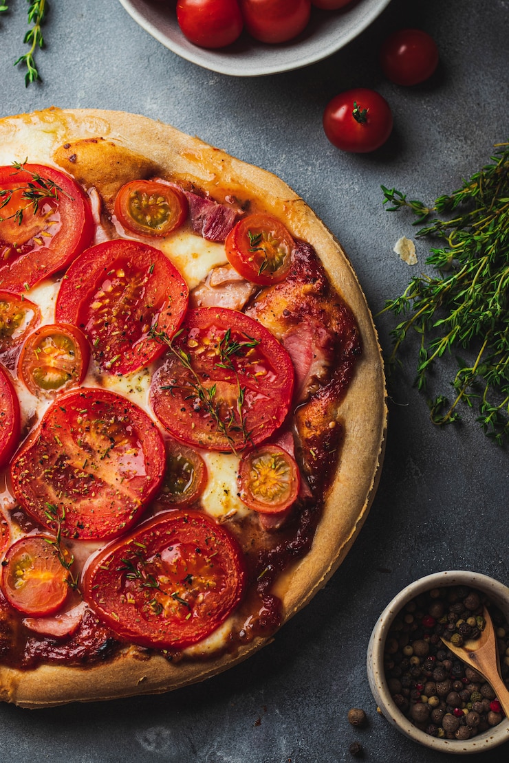 Foto gebackene pizza mit vollkornteig, tomate, schinken, mozzarella, tomatensauce, thymian serviert auf grauem steinhintergrund mit verschiedenen zutaten zum kochen.