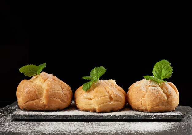 Gebackene Pudding-Eclairs, mit Puderzucker bestreut und mit einem Minzblatt auf einer Tafel verziert