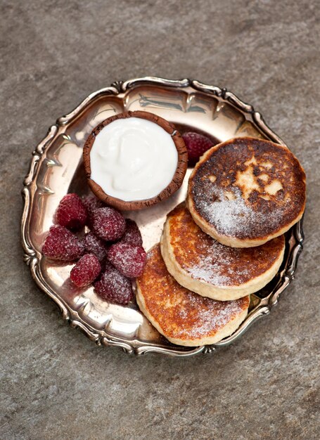 Gebackene Quarkpfannkuchen mit Sauerrahm und Himbeeren auf grauem Marmorhintergrund