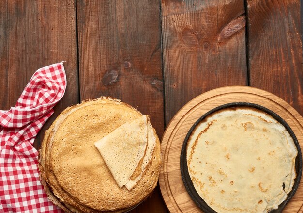 Gebackene runde dünne Pfannkuchen liegen gestapelt auf einem Holzbrett