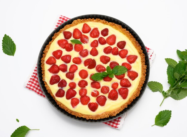 Gebackene runde Tarte mit Erdbeeren und zarter Milchcreme auf weißem Tischhintergrund, Ansicht von oben