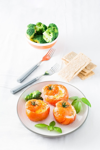 Gebackene Tomaten mit Ei, Brokkoli und Basilikumblättern auf einem Teller. Diät-Mittagessen. Vertikale Ansicht