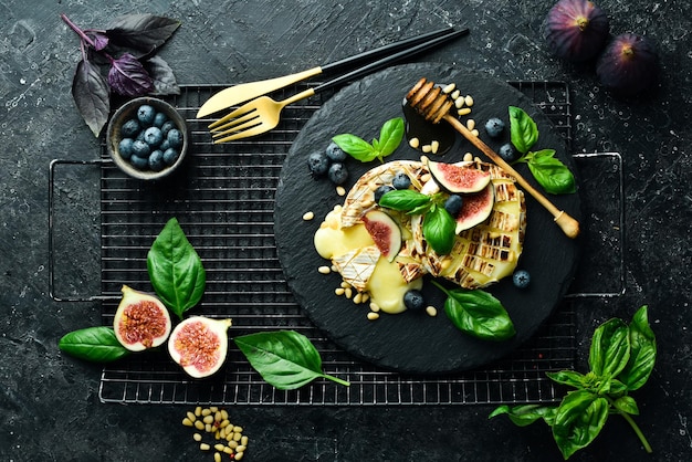 Gebackener Brie-Käse mit Feigen, Honig und Blaubeeren auf einem Teller auf schwarzem Hintergrund