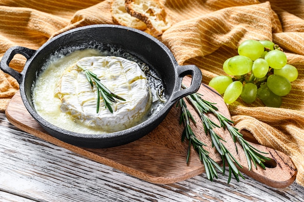 Gebackener Briekäse, Camembert mit Rosmarin in einer Pfanne. Weißer hölzerner Hintergrund. Draufsicht