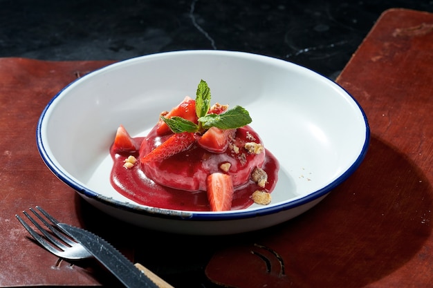 Gebackener Camembert-Käse mit Beerensauce und Erdbeeren in einem weißen Teller. Dunkle Oberfläche. Hartes Licht