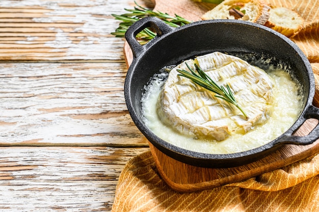 Gebackener Camembert mit Rosmarin in einer Pfanne. Weißer hölzerner Hintergrund. Draufsicht. Speicherplatz kopieren