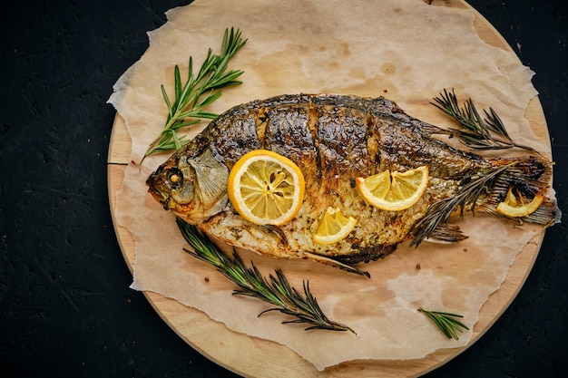 Gebackener Fisch im Ofen mit Zitrone und Rosmarin auf Schneidebrett und Pergamentpapier auf dunklem Hintergrund