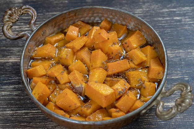 Gebackener gelber Kürbis mit Honig, Anis, Olivenöl und Gewürzen auf einem Teller auf dem Holztisch. Vegetarisches Essen. Nahaufnahme