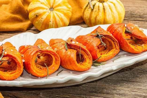 Gebackener Hokkaido-Kürbis mit Soßengewürzen und Honig, gesundes veganes Essen, trockener Rosmarin, moderner, harter, heller, dunkler Schatten, schwarzer Steinbetonhintergrund aus nächster Nähe