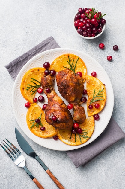 Gebackener Hühnertrommelstock mit Orangen und Moosbeeren in einem hellgrauen Hintergrund der Platte.