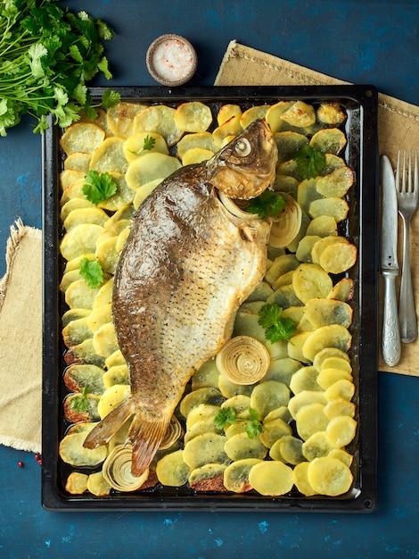 Gebackener Karpfen, ganzer Fisch aus dem Ofen mit geschnittenen Kartoffeln auf einem großen Tablett