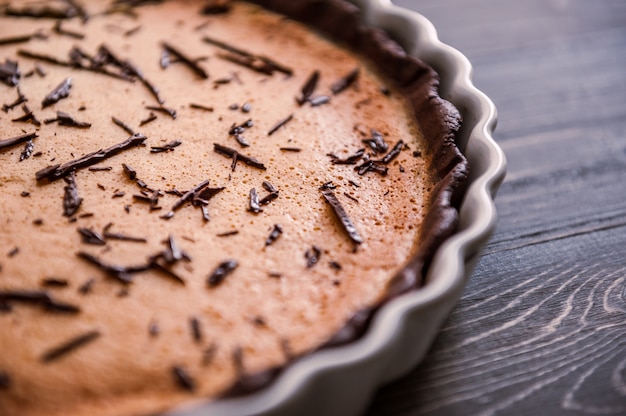 Gebackener Kuchen in einer keramischen Form besprüht mit Schokoladenscheiben auf einem Holztisch.