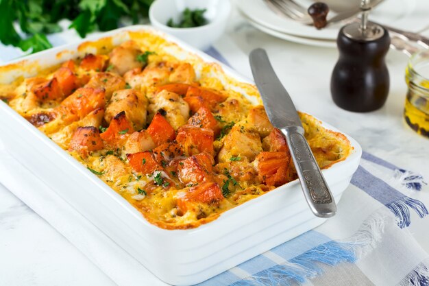 Gebackener Kürbis mit Huhn, Gewürzen und Sahnesauce in weißer Keramikform auf einem Leuchttisch. Selektiver Fokus.