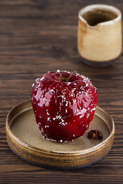 Gebackener roter Apfel mit Walnüssen und Honig in roter Glasur mit Kokosflocken auf einem Holztisch.