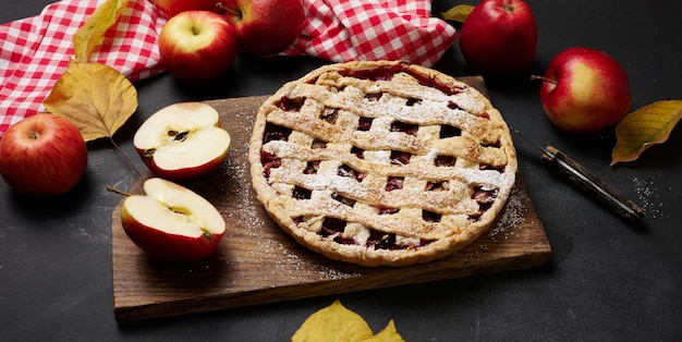 Gebackener runder traditioneller Apfelkuchen auf braunem Holzbrett und Draufsicht der frischen roten Äpfel