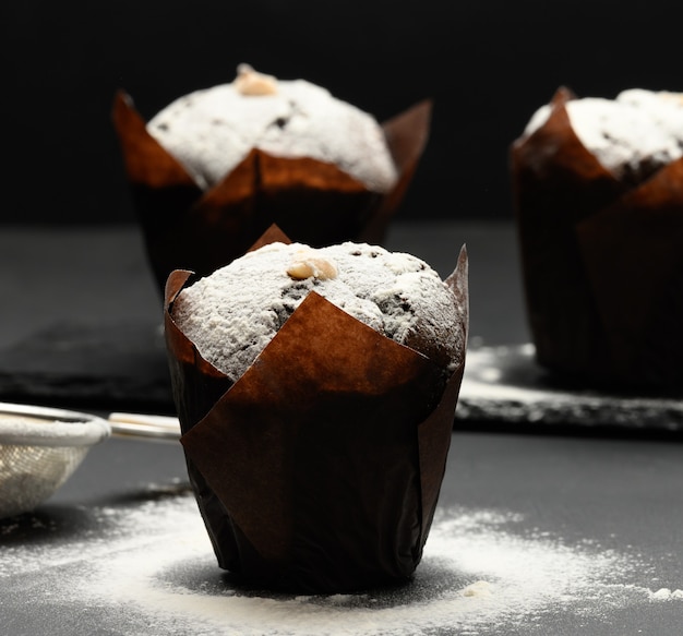 Gebackener Schokoladenmuffin mit Sahnefüllung, bestreut mit Puderzucker auf einem schwarzen Tabl