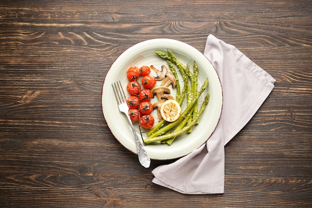 Gebackener Spargel mit Kirschtomaten und Zitrone auf dem Teller auf einer Holzoberfläche. Ansicht von oben