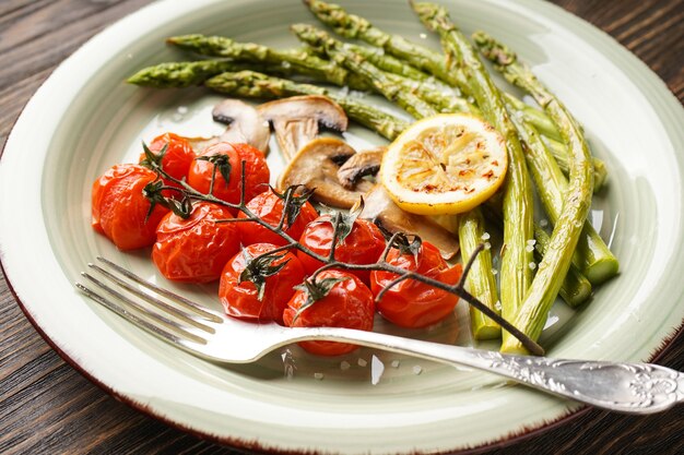 Gebackener Spargel mit Kirschtomaten und Zitrone in einem Teller auf einer Holzoberfläche, Nahaufnahme.