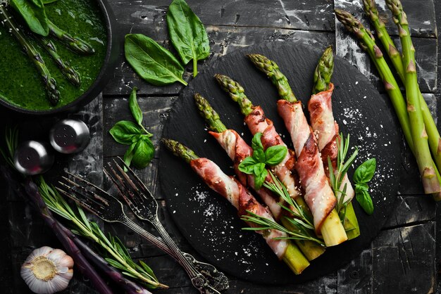 Gebackener Spargel mit Speck und Gewürzen auf einer schwarzen Steinplatte Draufsicht Freier Platz für Ihren Text