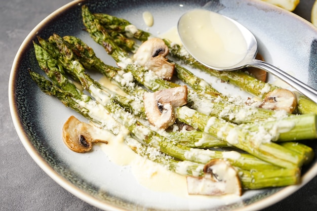 Gebackener Spargel und Pilze mit Sauce in einem Teller auf grauem Hintergrund. Nahansicht.