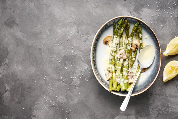 Gebackener Spargel und Pilze mit Sauce in einem Teller auf grauem Hintergrund, Platz für Text. Flach liegen.