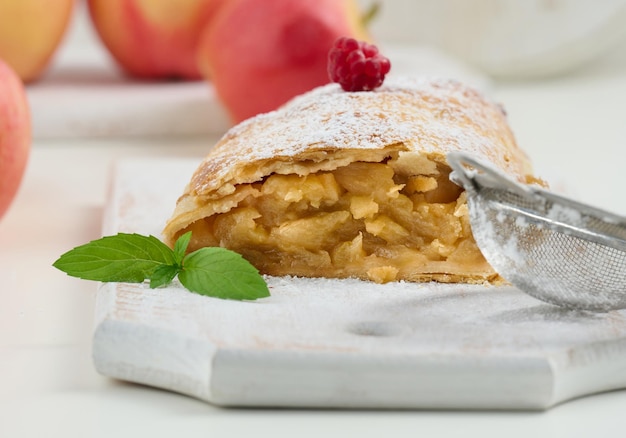 Gebackener Strudel mit mit Puderzucker bestreuten Äpfeln auf einem weißen Holzbrett