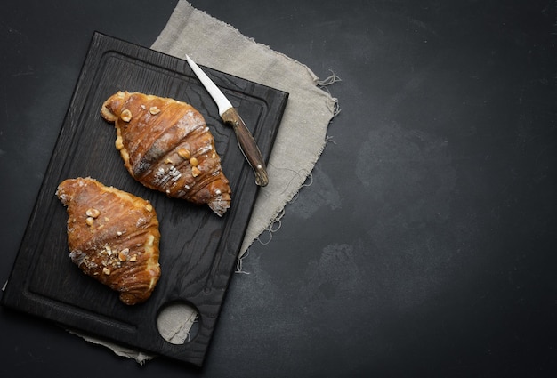 Gebackenes Croissant auf einem Brett und mit Puderzucker bestreut schwarzer Tisch Appetitliches Gebäck zum Frühstückx9