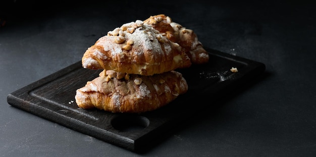 Gebackenes Croissant auf einem Brett und mit Puderzucker bestreut schwarzer Tisch Appetitliches Gebäck zum Frühstückx9